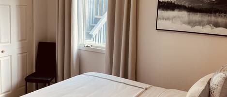 Ein Schlafzimmer mit einem Bett, einem Sessel, einem Fenster mit Vorhängen und einem Bild an der Wand.