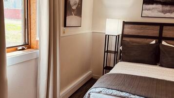 A bedroom with a wooden bed, a window with curtains, and two framed pictures on the wall.