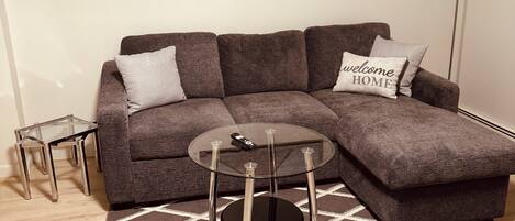 A modern living room with a sectional sofa, a glass coffee table, and a geometric patterned rug.
