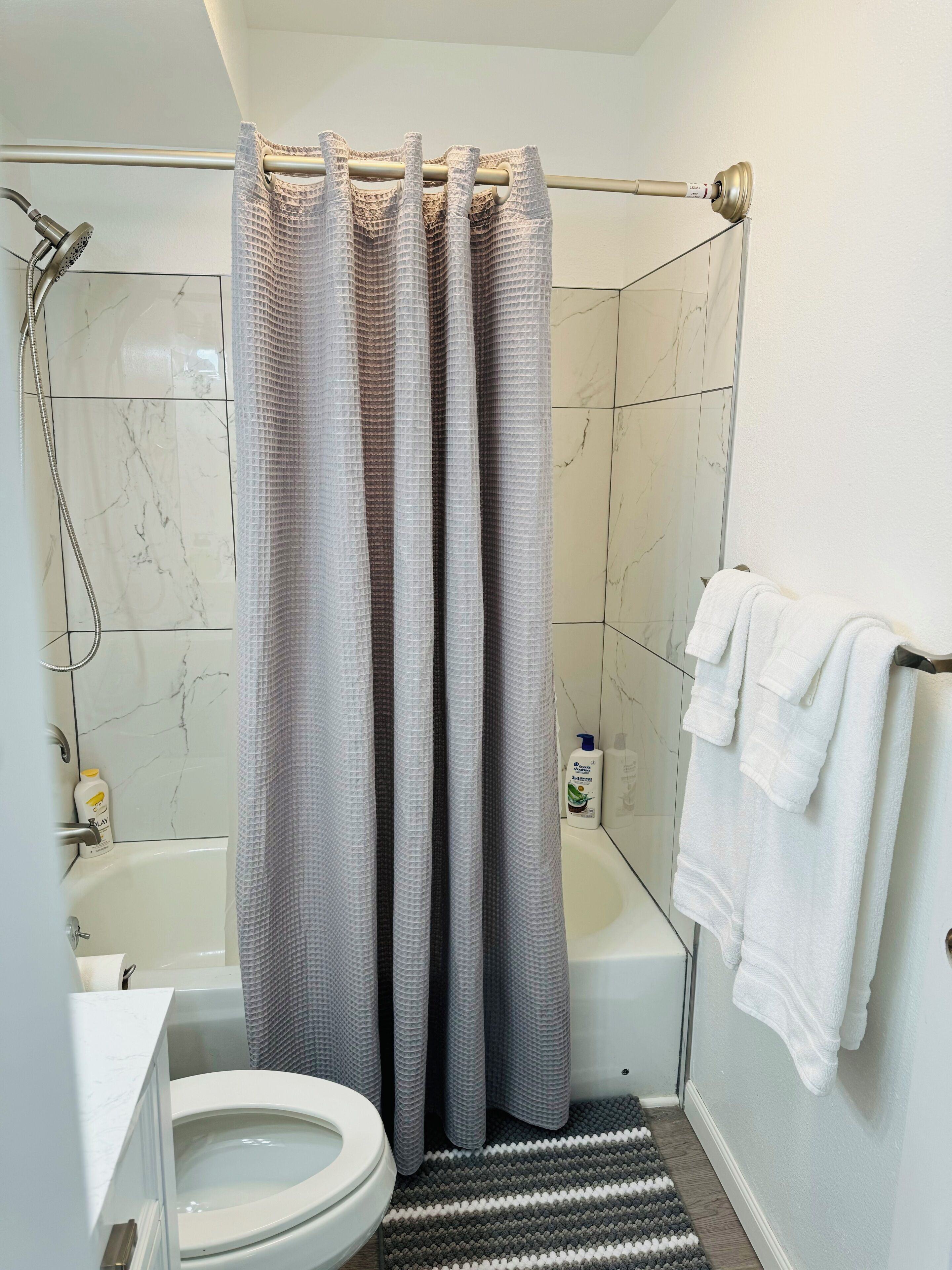 A bathroom with a shower curtain, a bathtub, a toilet, and a striped rug.