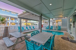 An outdoor pool area with picnic tables and chairs, surrounded by a white fence and a building with balconies.