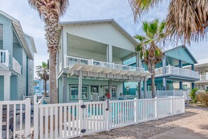 A beachfront hotel with a covered porch, white railings, and a pool.