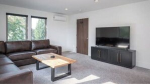 Een moderne woonkamer met een modulaire bank, een houten salontafel, een flatscreen-televisie en een donkere tv-meubel.