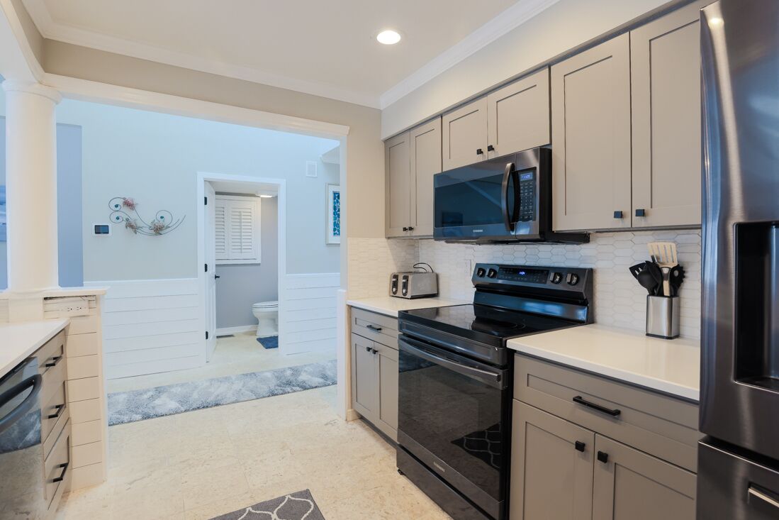 A modern kitchen with stainless steel appliances, light-colored cabinetry, and a visible door leading to another room.