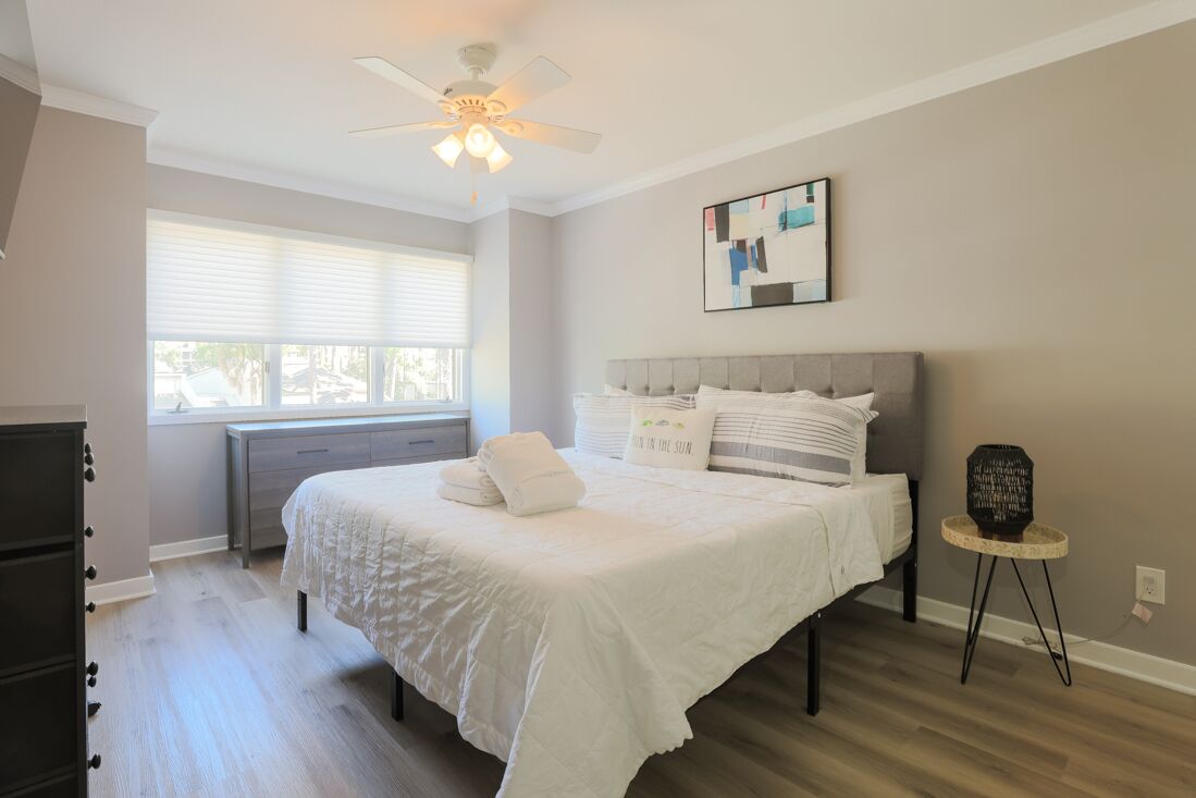 Une chambre à coucher comprenant un lit, un ventilateur de plafond, une fenêtre et une œuvre d’art accrochée au mur.