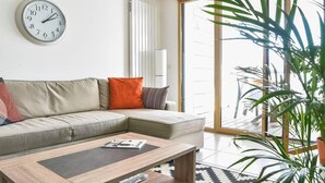 Una sala de estar moderna con un sofá modular, una mesa de centro, un reloj y un ventanal grande.