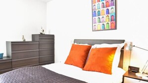 Un dormitorio ordenado con cama, cómoda y mesita de noche.