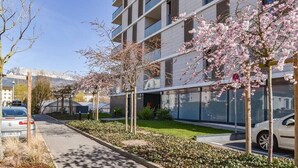 Un edificio moderno con fachada de vidrio, un área de estacionamiento y árboles de cerezo.