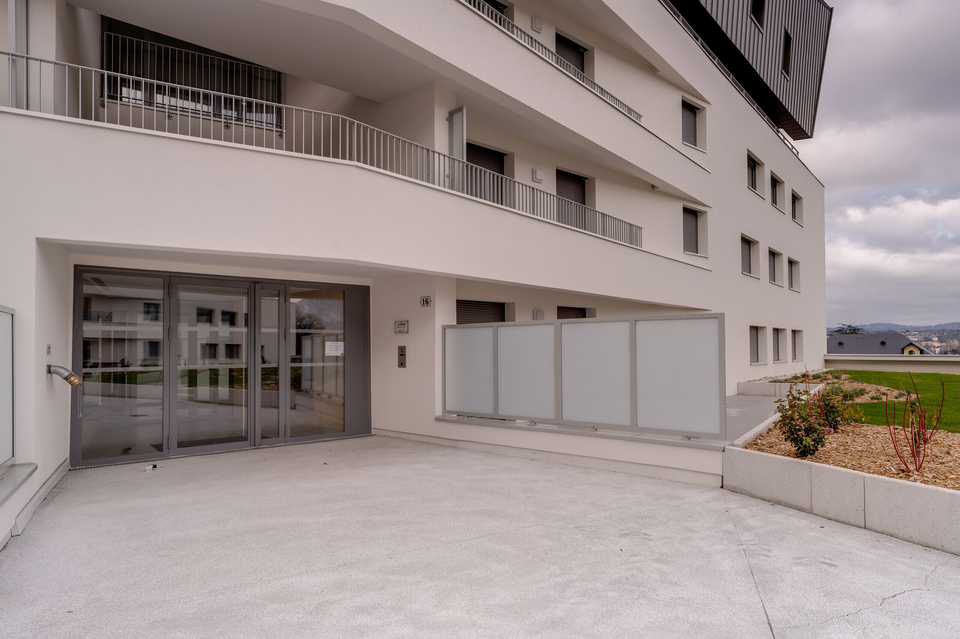 Un bâtiment moderne doté d’une entrée en verre, de nombreux balcons et offrant une vue sur un paysage verdoyant.