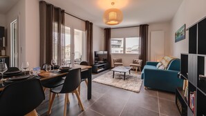 A modern living room with a dining area, large windows, and a blue sofa. - Le 305 - T3 with garage and beautiful terrace (Annecy)