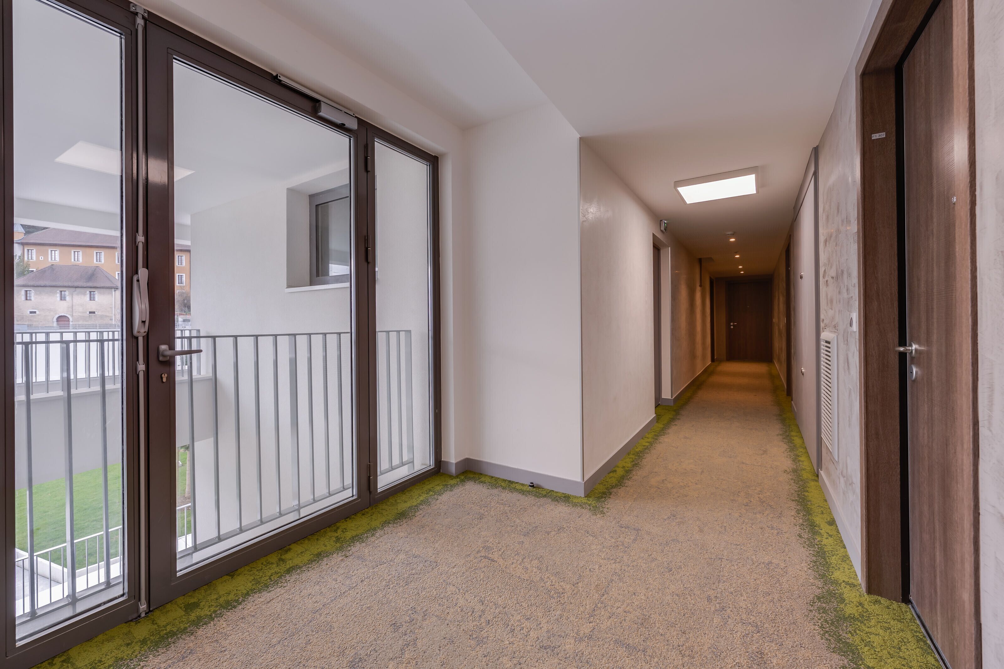 Ein Korridor mit Schiebeglasüren zu einem Balkon, einem Teppichboden und einer Deckenleuchte.