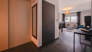 A modern living room with a dark wooden door, a dining area with a table and chairs, and a large window with curtains. - Le 305 - T3 with garage and beautiful terrace (Annecy)