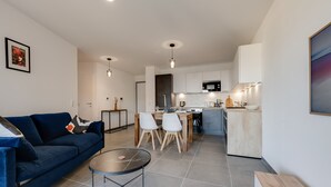 Una sala de estar moderna con un sofá azul, una mesa de centro y un comedor con sillas, y una cocina al fondo.