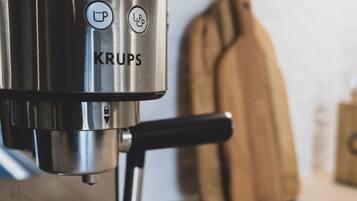 A Krups coffee machine with a black drip tray and a wooden cutting board in the background.
