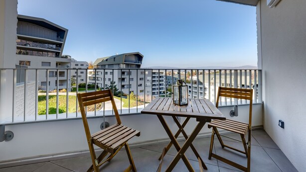 Un balcón con mesa y sillas, con vistas a una zona residencial con edificios modernos.