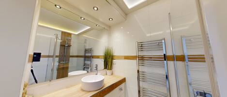 Un baño moderno con un espejo grande, dos lavamanos, una ducha y un perchero para toallas.