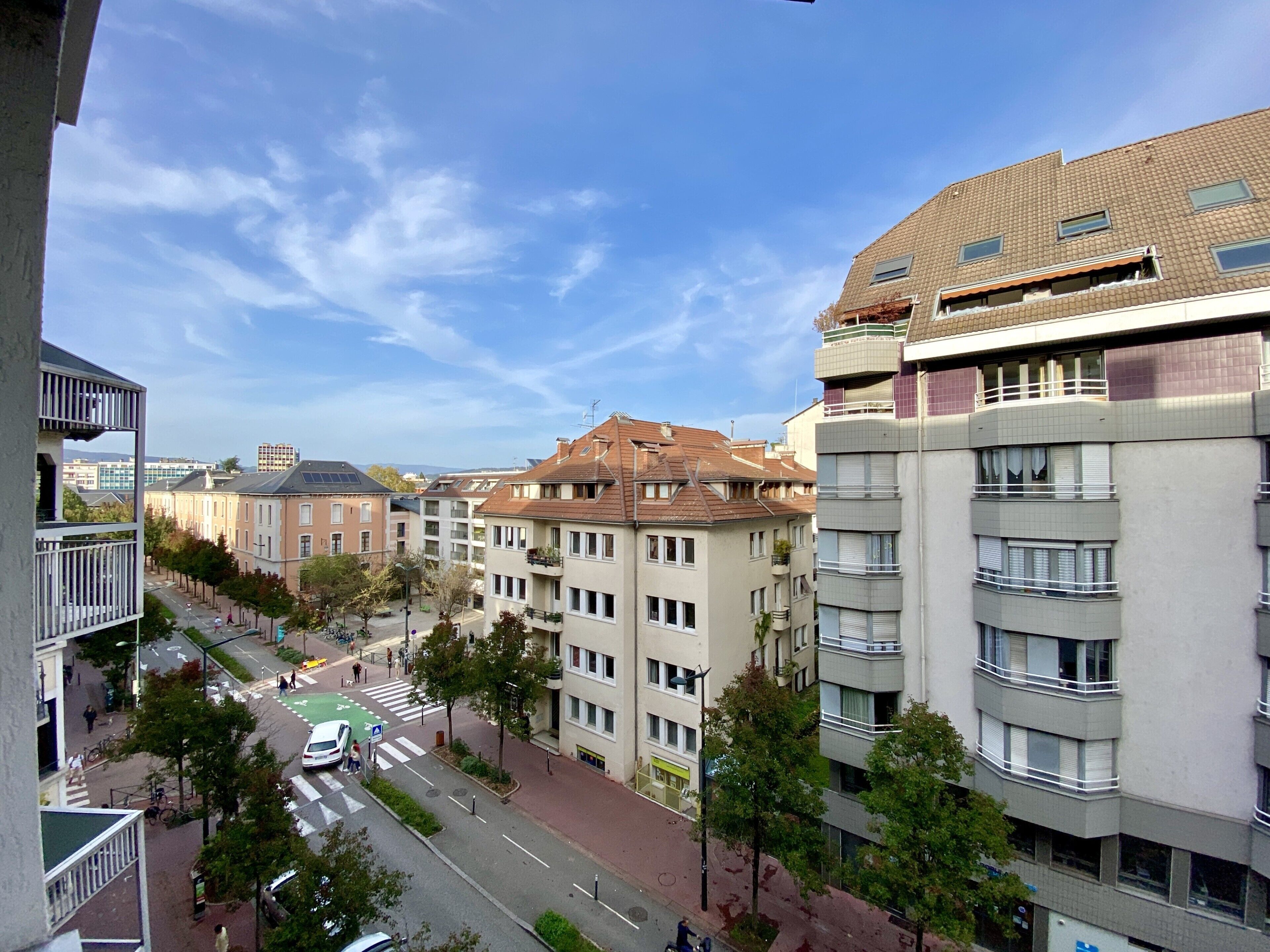 A multi-story residential building with balconies, a pedestrian street, and a crosswalk.