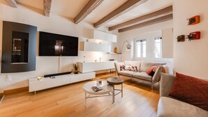 Una sala de estar moderna con un televisor de pantalla plana, muebles blancos, una mesa de centro redonda y un sofá con almohadones decorativos.