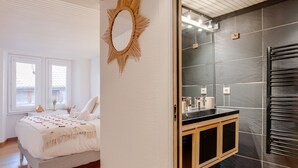 Un dormitorio con cama, un baño con toallero y un espejo con forma de sol en la pared.