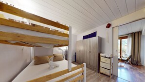 A bunk bed with a wooden frame and white bedding, a wardrobe with sliding doors, and a chair by a window.