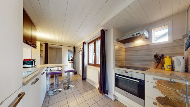 A modern kitchen with a built-in oven, a dining area with bar stools, and a window providing natural light.