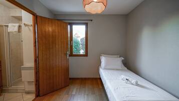 A small, clean room with a wooden door, a window, a bed, and a shower area.