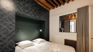 A neatly made bed with pillows and towels, a headboard with a geometric pattern, a bedside lamp, and a window with curtains. - L'Appart' - Ideal for a stay in the city center, near the Lake (Annecy)