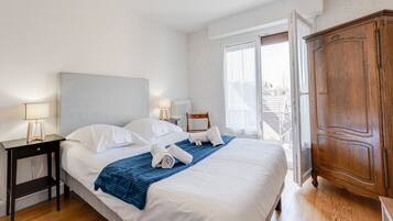 A neatly made bed with white linens and a blue blanket, a wooden nightstand with a lamp, and a large wooden wardrobe.