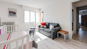 Una sala de estar moderna con un sofá gris, un banco de madera pequeño, un radiador blanco y un cuadro enmarcado en la pared.