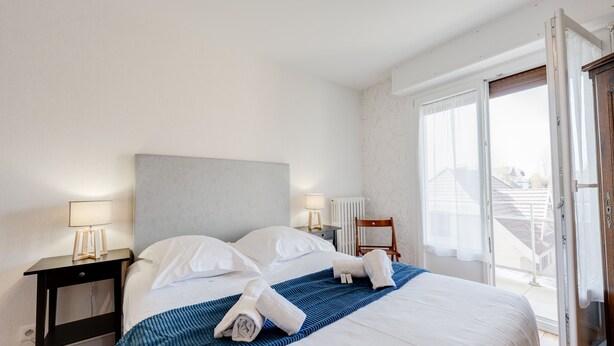 Habitación de hotel con cama, dos mesitas de noche con lámparas, un radiador y vistas al exterior.