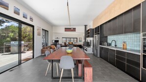 A modern kitchen with a long dining table, dark cabinetry, and a view of the outdoors.
