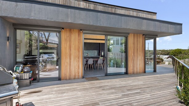 A modern house with a deck, sliding glass doors, and a barbecue grill outside.