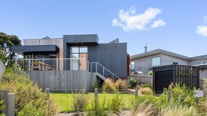 A modern two-story house with a covered outdoor area, a visible staircase, and a fenced yard.