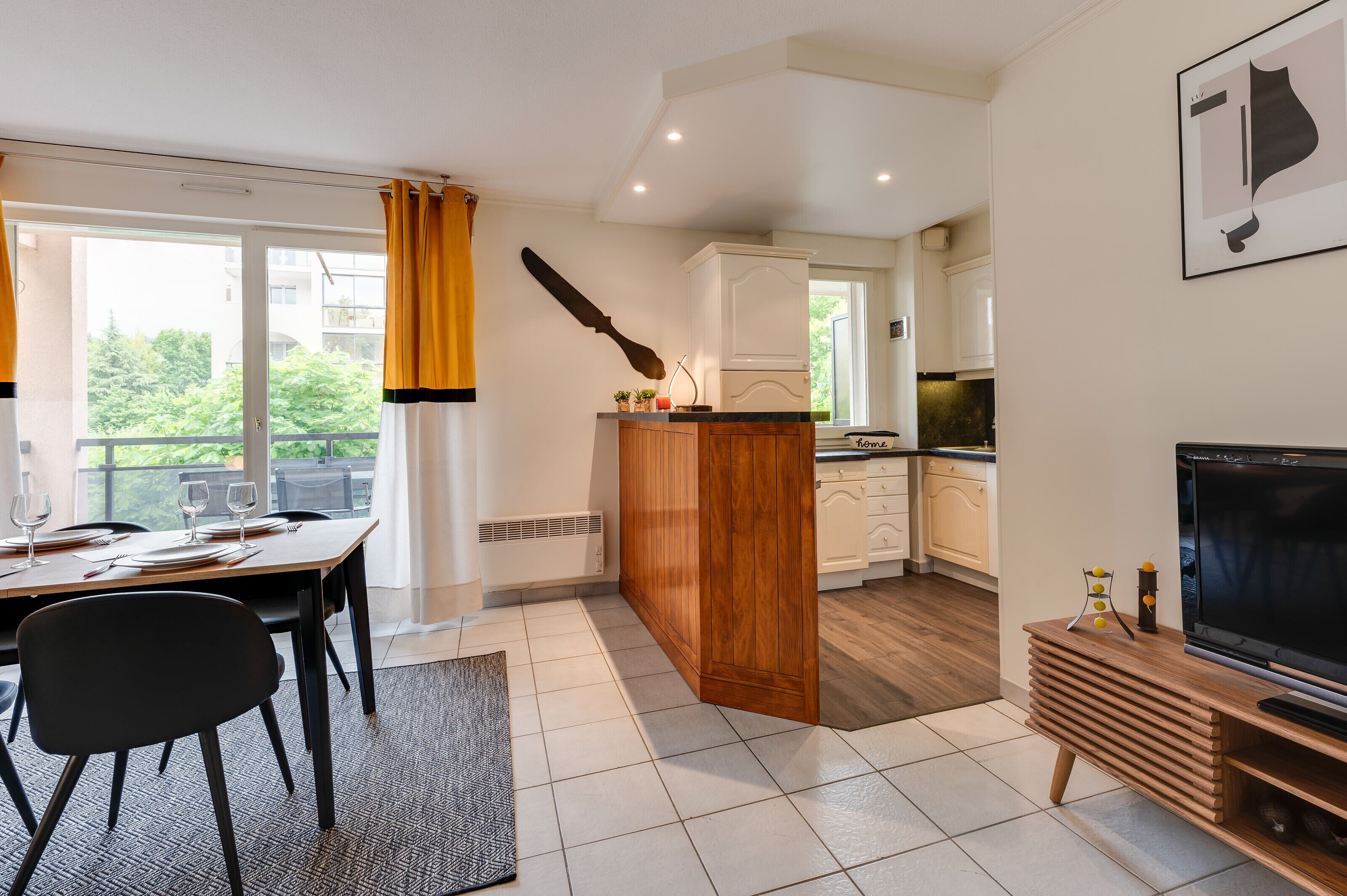 Una cocina moderna con armarios blancos, una isla de madera y un comedor con una mesa dispuesta para dos.