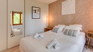 A neatly made bed with white linens and pillows, a bedside table with a lamp, and a wall-mounted artwork. - The Parc des Raisses - T2 for 4 people (Annecy)