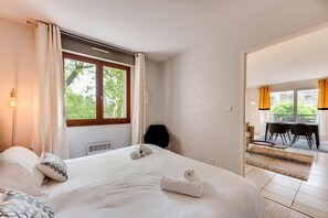 A hotel room with a bed, a chair, a table, and a view of the outdoors.