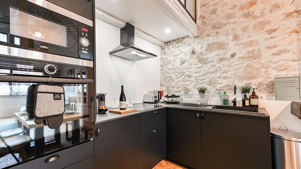 Une cuisine moderne avec un mur en pierre, un four encastré et un plan de travail en bois.