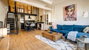Un salon spacieux doté d’un plancher en bois, d’un canapé bleu, d’une table basse et d’un escalier menant à un niveau supérieur.