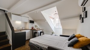 Un studio compact comprenant un coin cuisine, un lit avec des oreillers, un escalier et une lucarne.