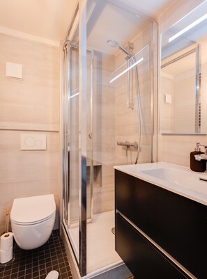 Une salle de bain moderne avec une douche à parois de verre, des toilettes blanches et un meuble-lavabo noir avec un miroir.