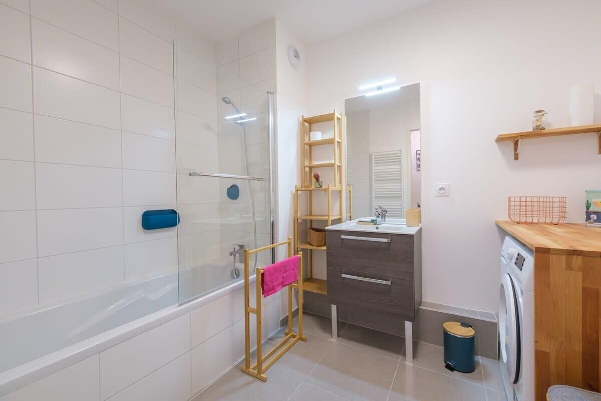 Ein modernes Badezimmer mit einer Duschkabine aus Glas, einem hölzernen Wäscheständer, einem Waschbecken mit Spiegel und einer Waschmaschine.