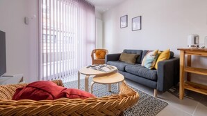 Ein modernes Wohnzimmer mit grauem Sofa, einem Korbstuhl, einem kleinen runden Tisch und einem Couchtisch.