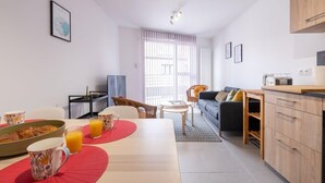 Ein modernes Wohnzimmer mit Essbereich, einer Couch, einem Fernseher und einer Küche mit Holzausbau.