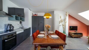 A modern kitchen with a dining area, including a wooden table set for four, a coffee machine, and a TV in the living area. - The Azalea, beautiful quiet apartment for 4 people! (Doussard)