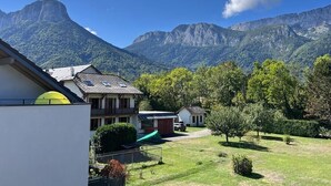 A mountain landscape with a clear sky, a building with a sloped roof, and a green field. - The Azalea, beautiful quiet apartment for 4 people! (Doussard)
