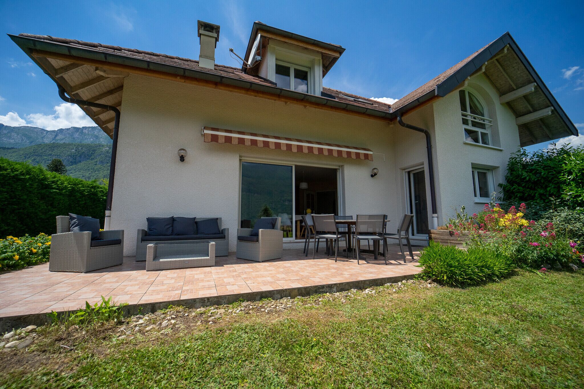 A two-story house with a patio, outdoor furniture, and a garden.