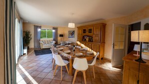 A dining area with a round table set for six, surrounded by white chairs. There is a wooden cabinet with glass doors to the right, and a door leading to another room. - Entre lac et montagnes (Doussard)