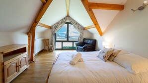 A bedroom with a large bed, a wooden dresser, a chair, and a view of a snowy landscape through a window. - Entre lac et montagnes (Doussard)