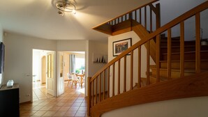 A staircase with wooden railings leading to an upper floor. A dining area with a table and chairs is visible in the background. - Entre lac et montagnes (Doussard)