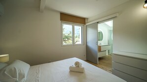 Quarto com cama, janela, porta para um banheiro e abajur.